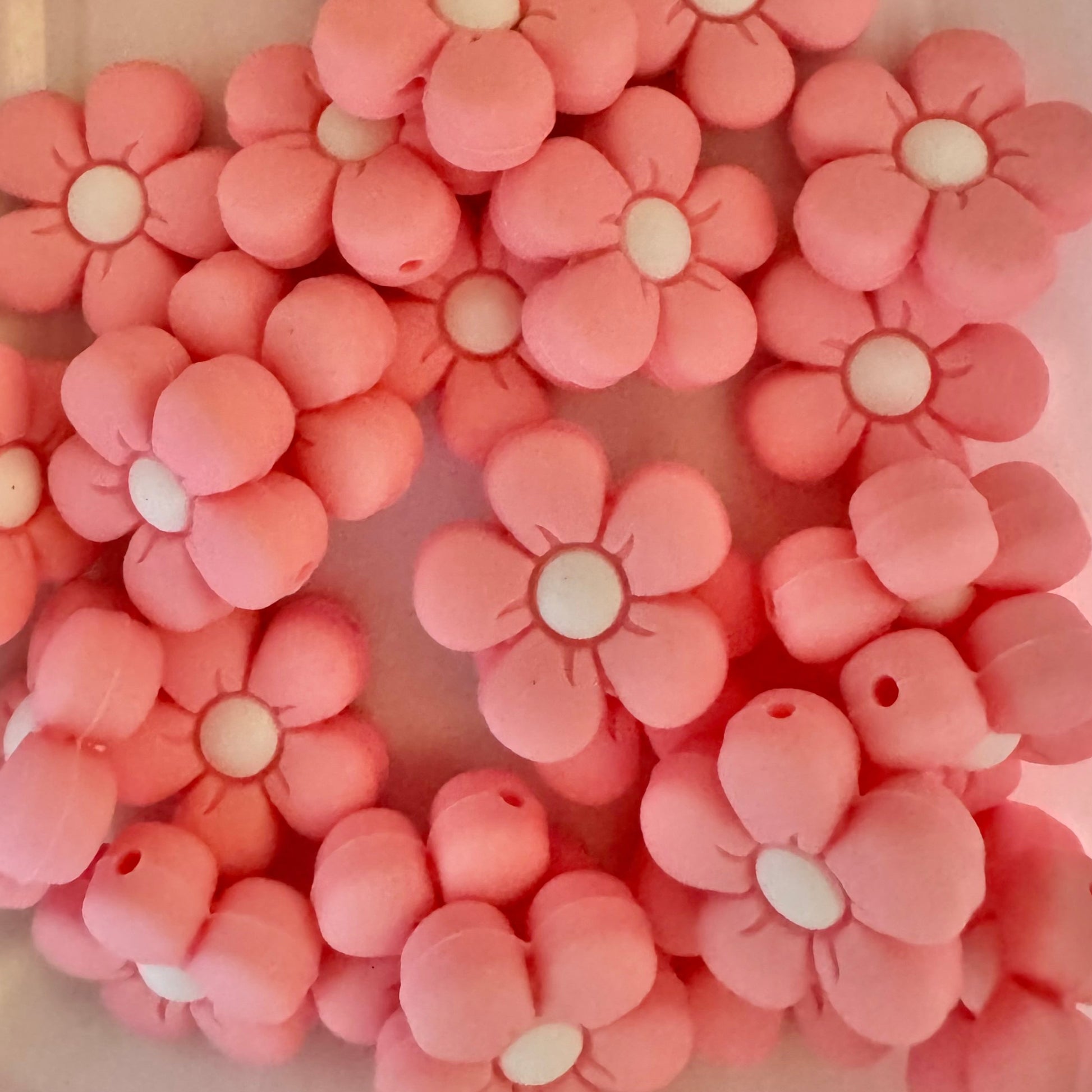Pink flower-shaped beads with white centers on a light pink background