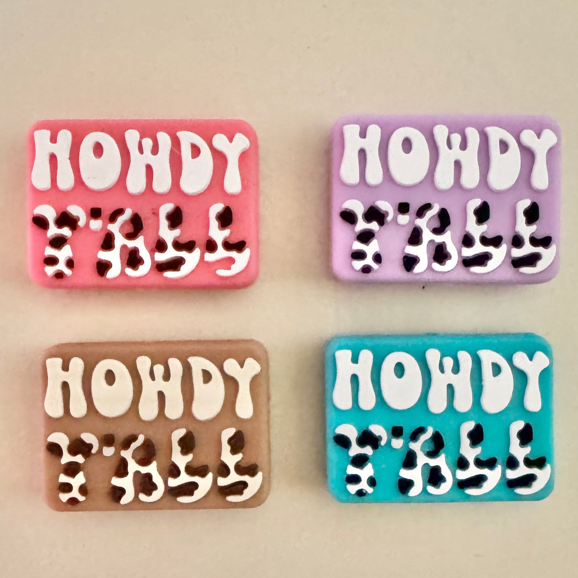 Four colorful 'HOWDY' beads with cow print on a beige background