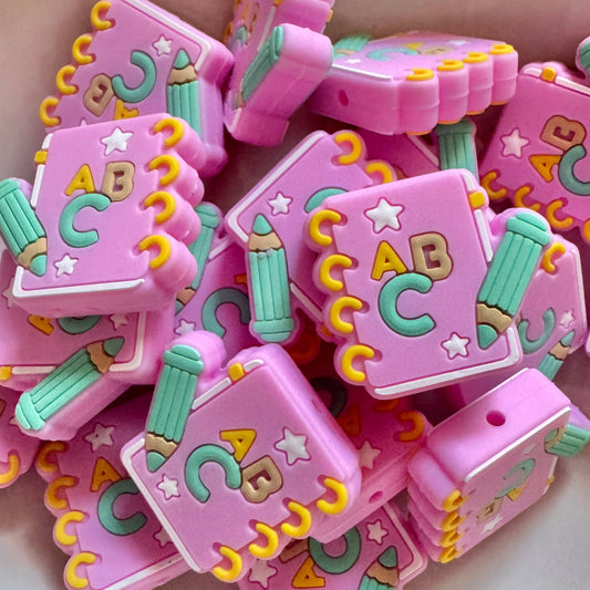 Pink bead with 'ABC' and colorful designs on a white surface