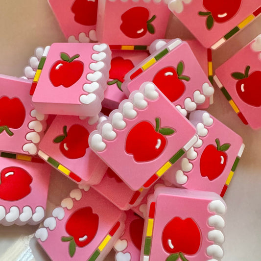 Pink square silicone bead with red apple designs on a white plate