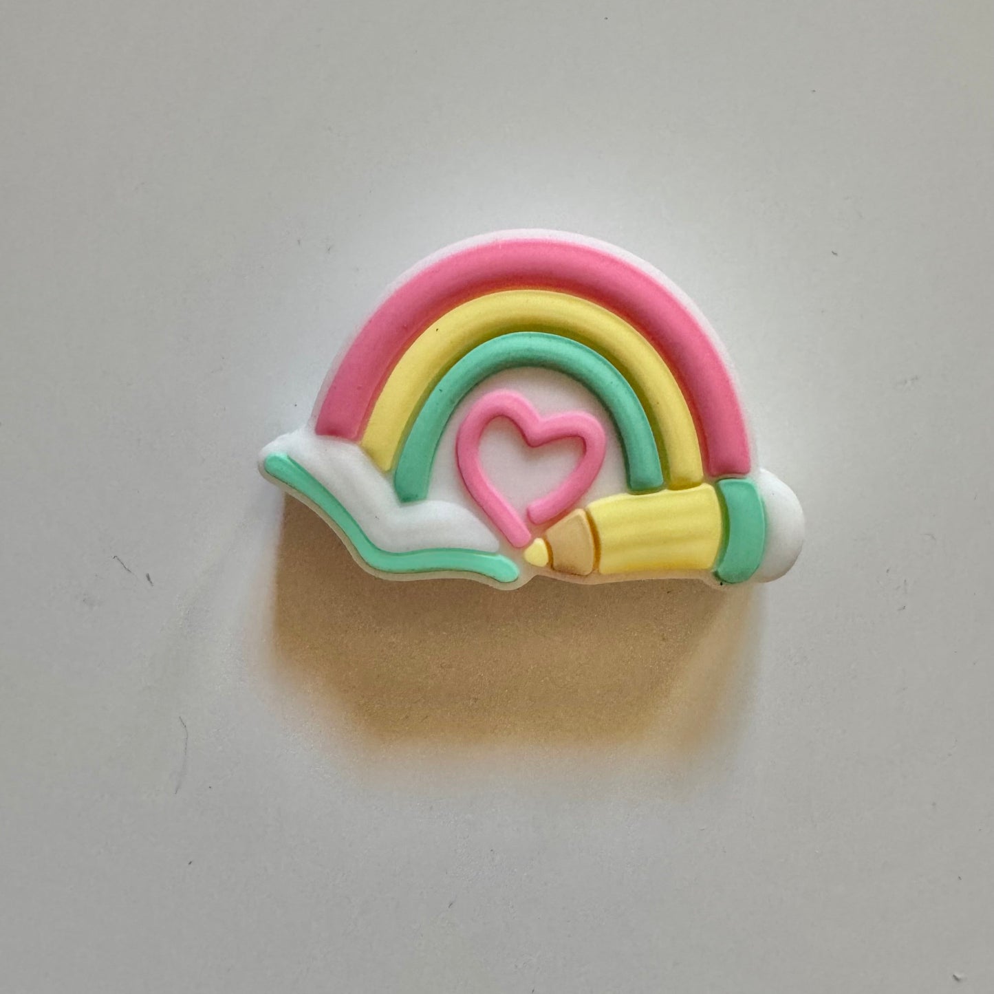 Colorful rainbow-shaped bead with a heart in the center on a light gray background