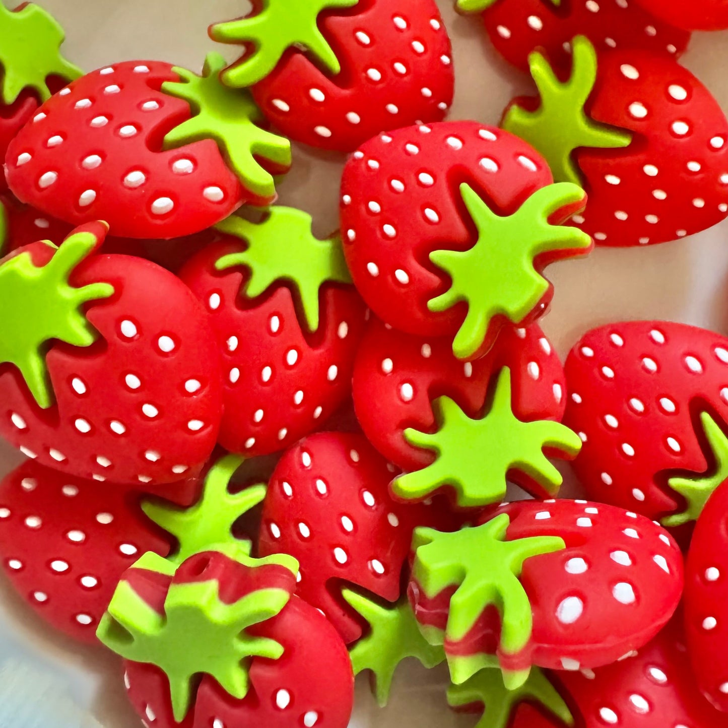 Red strawberry-shaped objects with green leaves on a beige surface