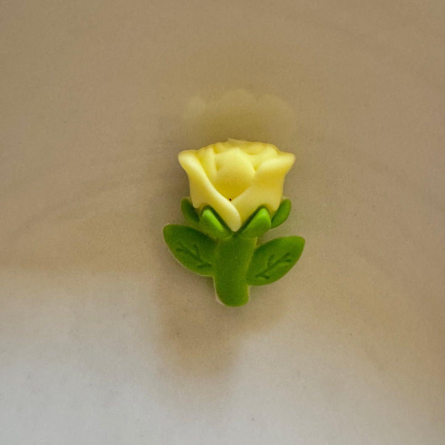 Small yellow rose with green leaves on a beige background